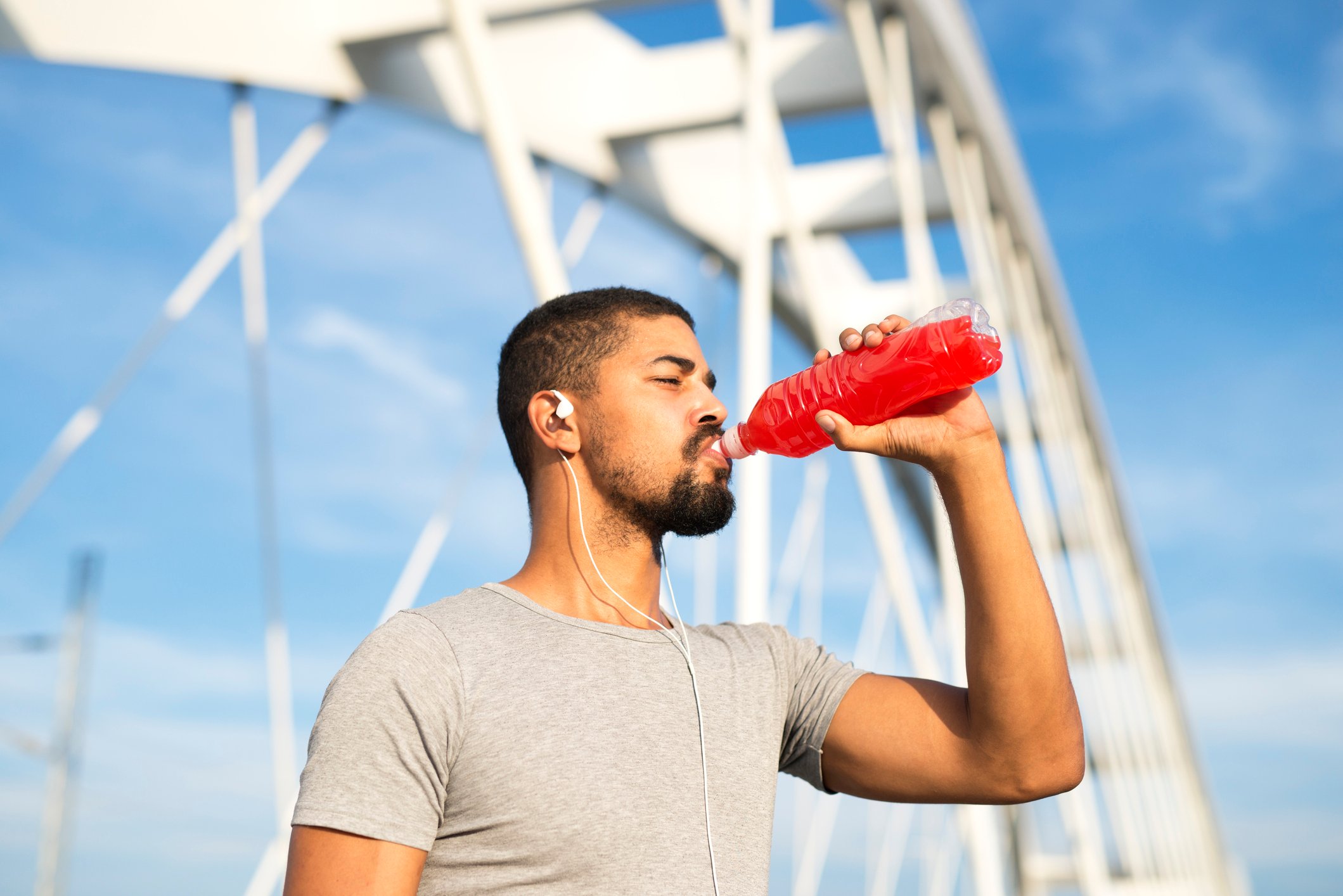 Man drinking red energy drink while standing beside bridge