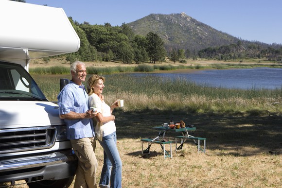 A couple standing in front of their RV are enjoying the outdoors.