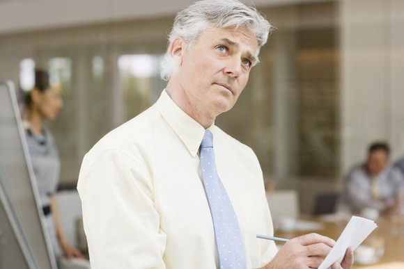 Older man in dress shirt and tie writing on piece of paper