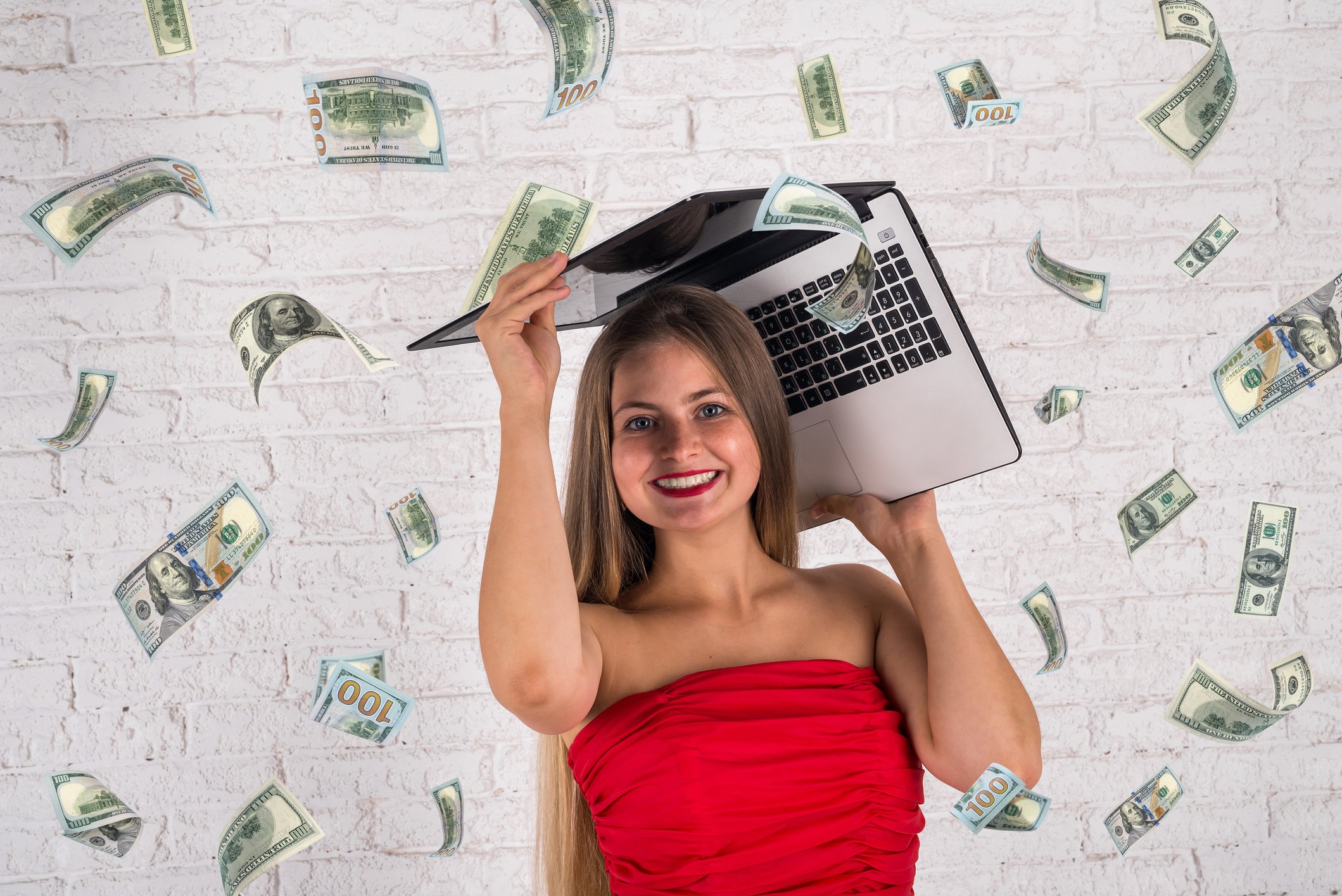 $100 bills raining down on a woman holding a laptop over her head