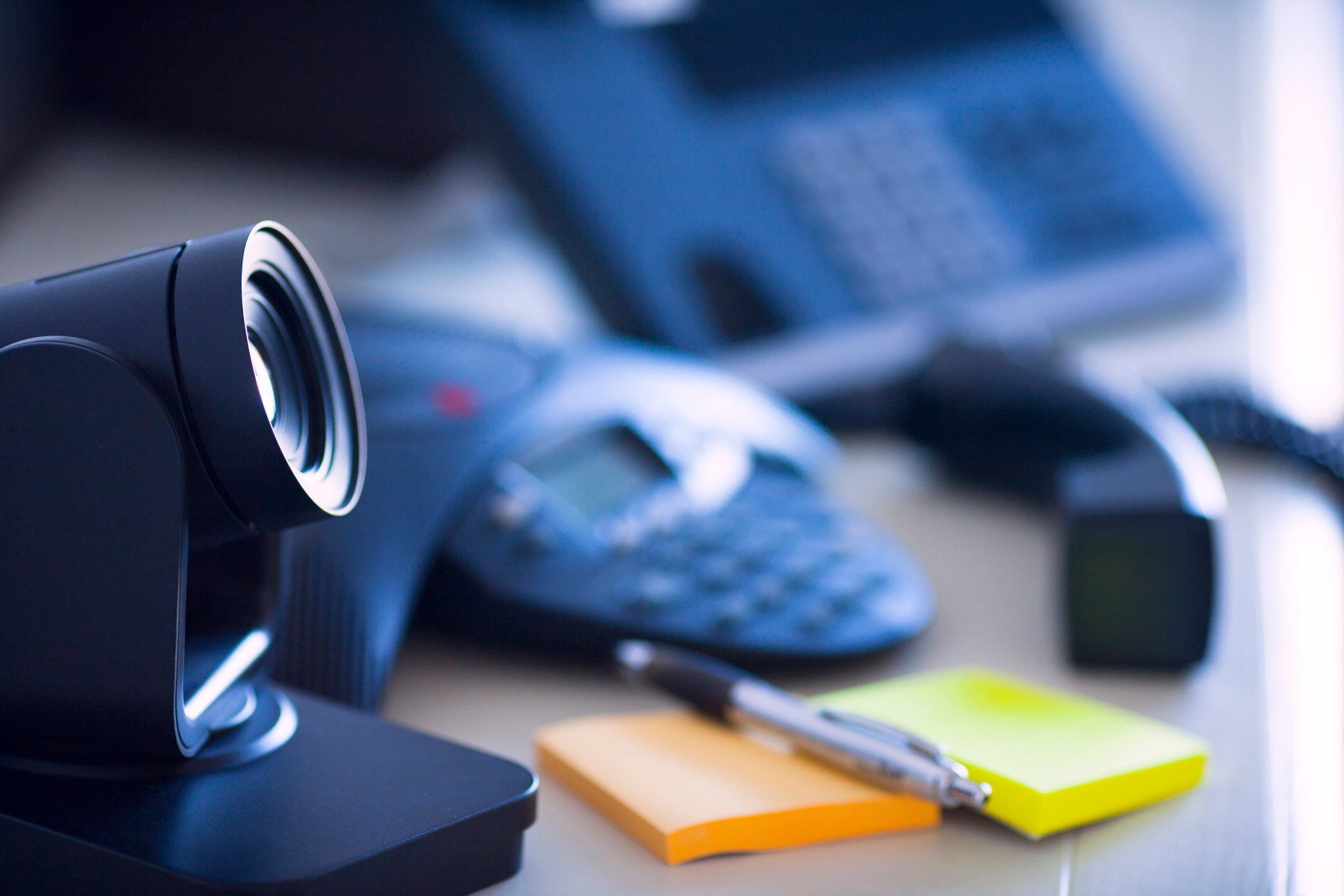 A PC webcam, notepad, and phone sitting on a desk.