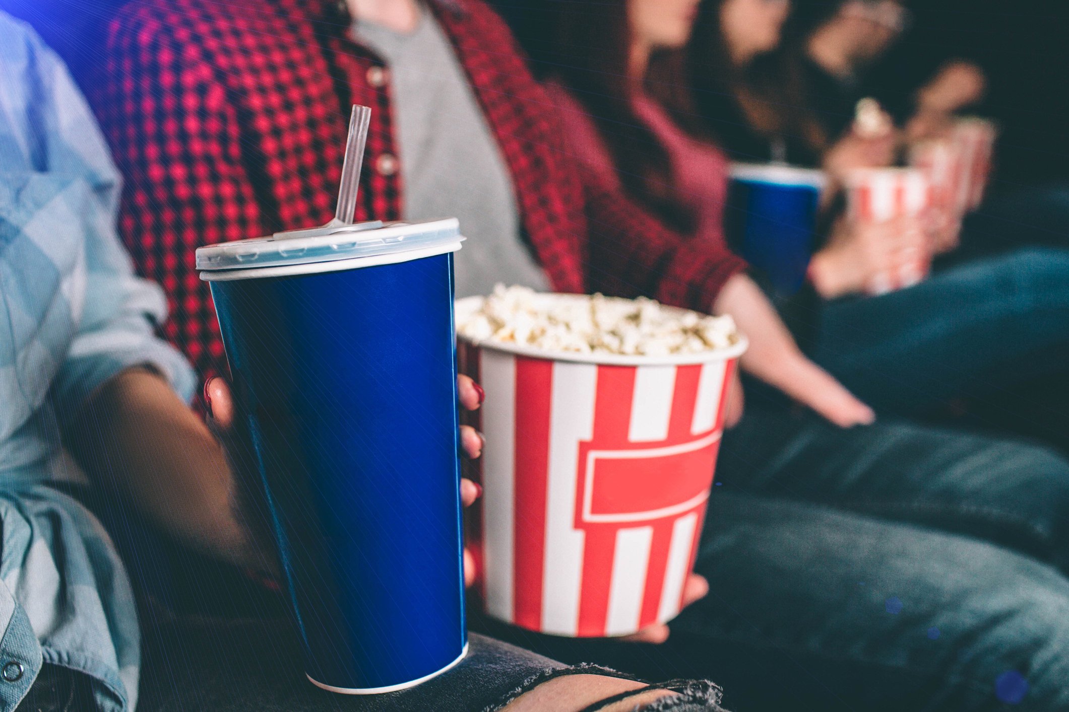 Patrons at a movie theater, one holding a bucket of popcorn and the other a soft drink.