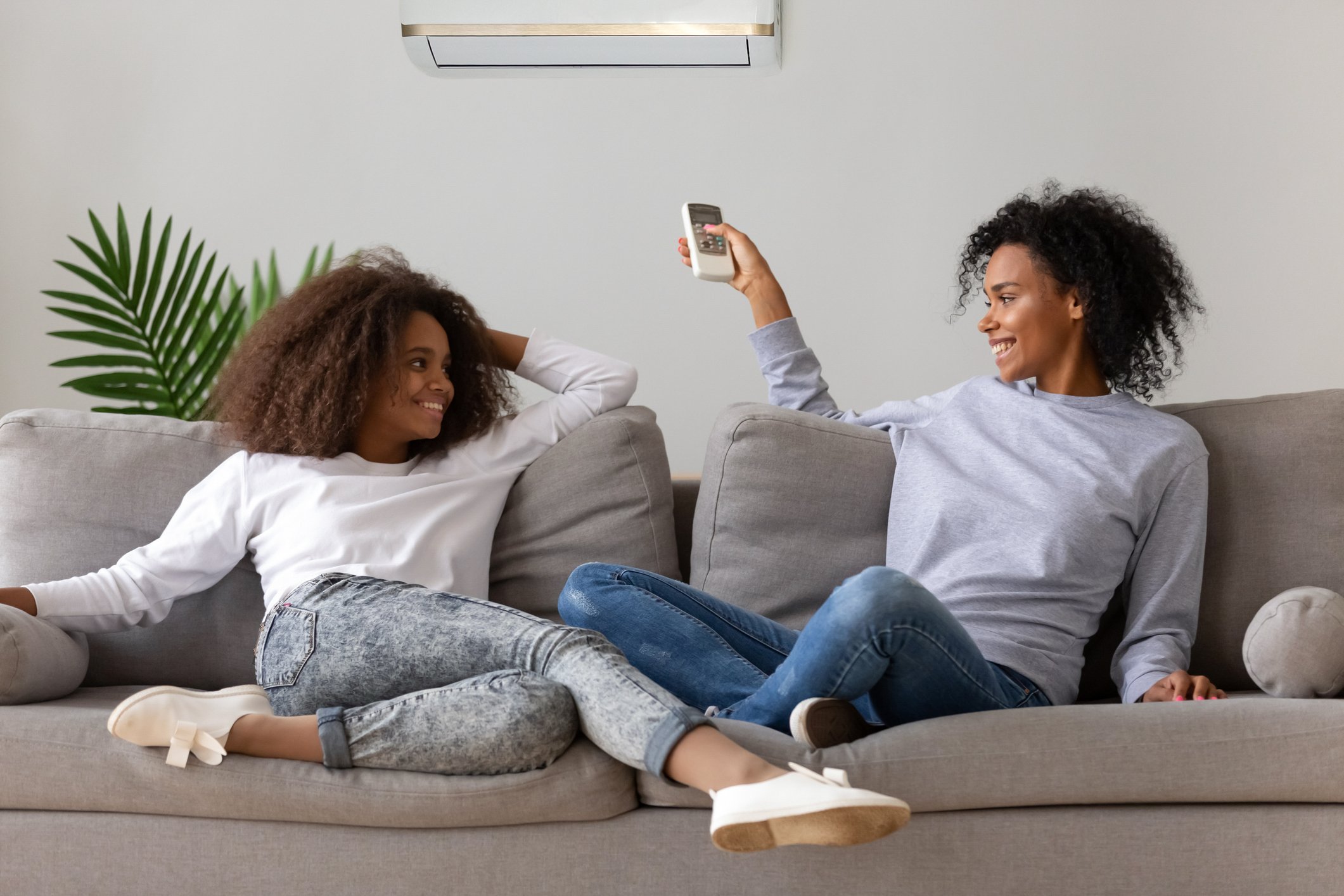 Two women sit on a couch near an air conditioning unit.