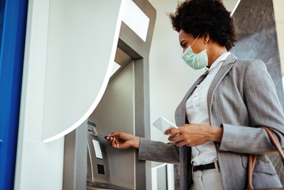 A woman in a mask uses an ATM.
