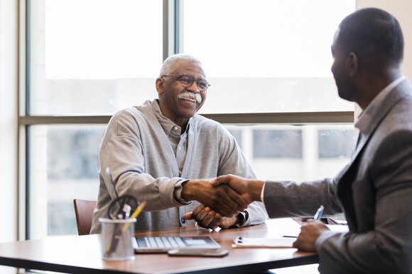 A senior man shakes hands with a retirement professional. 
