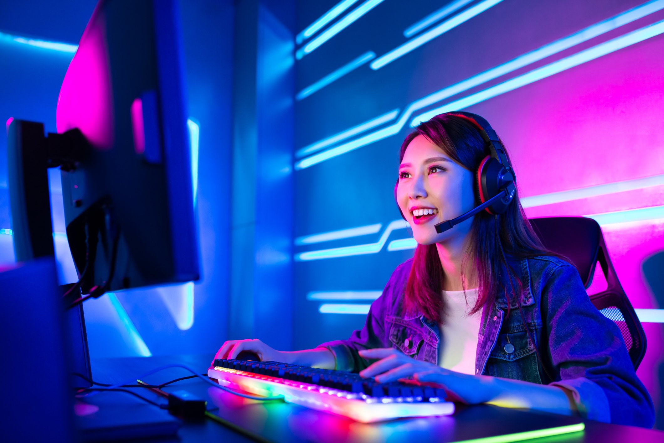 Young woman in a dark room wearing headset at a gaming computer with a multicolor keyboard