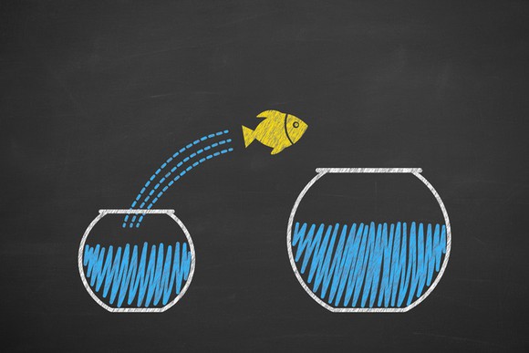 A fish jumping from a small fishbowl to a larger one.