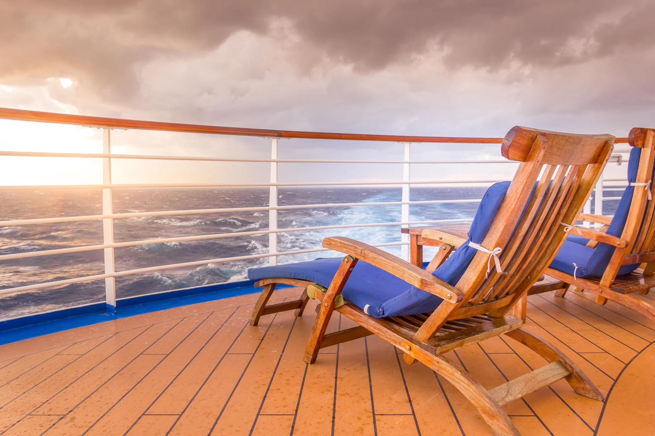 Two deck chairs on a wooden deck on a ship, overlooking sunset and ship wake.