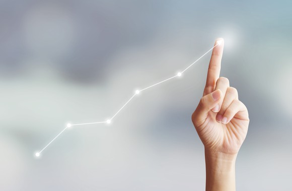 A finger traces an upward-trending line, suggestive of a rising stock chart.