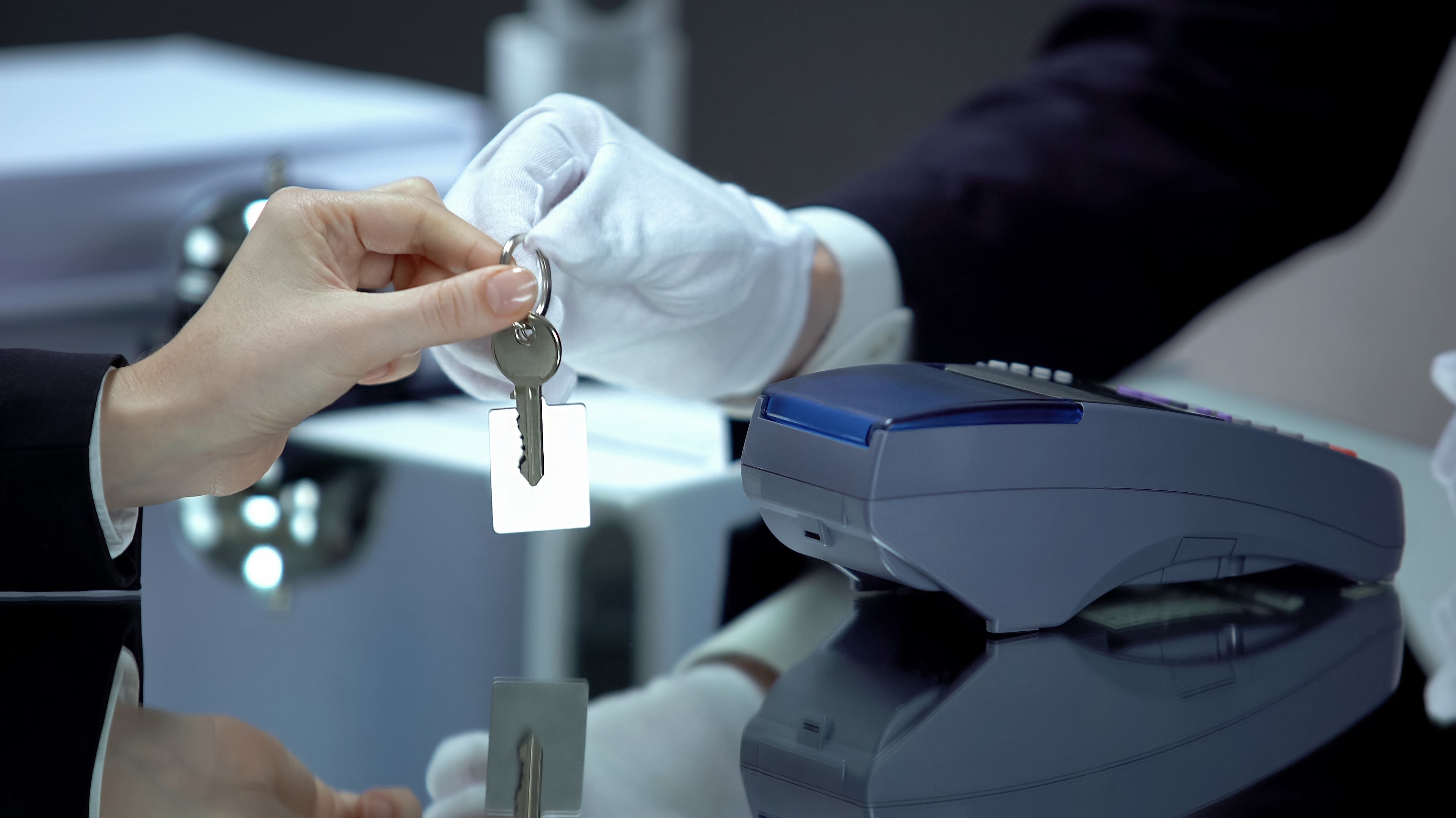 A gloved hotel receptionist hands over a key to a traveler after a contactless payment.
