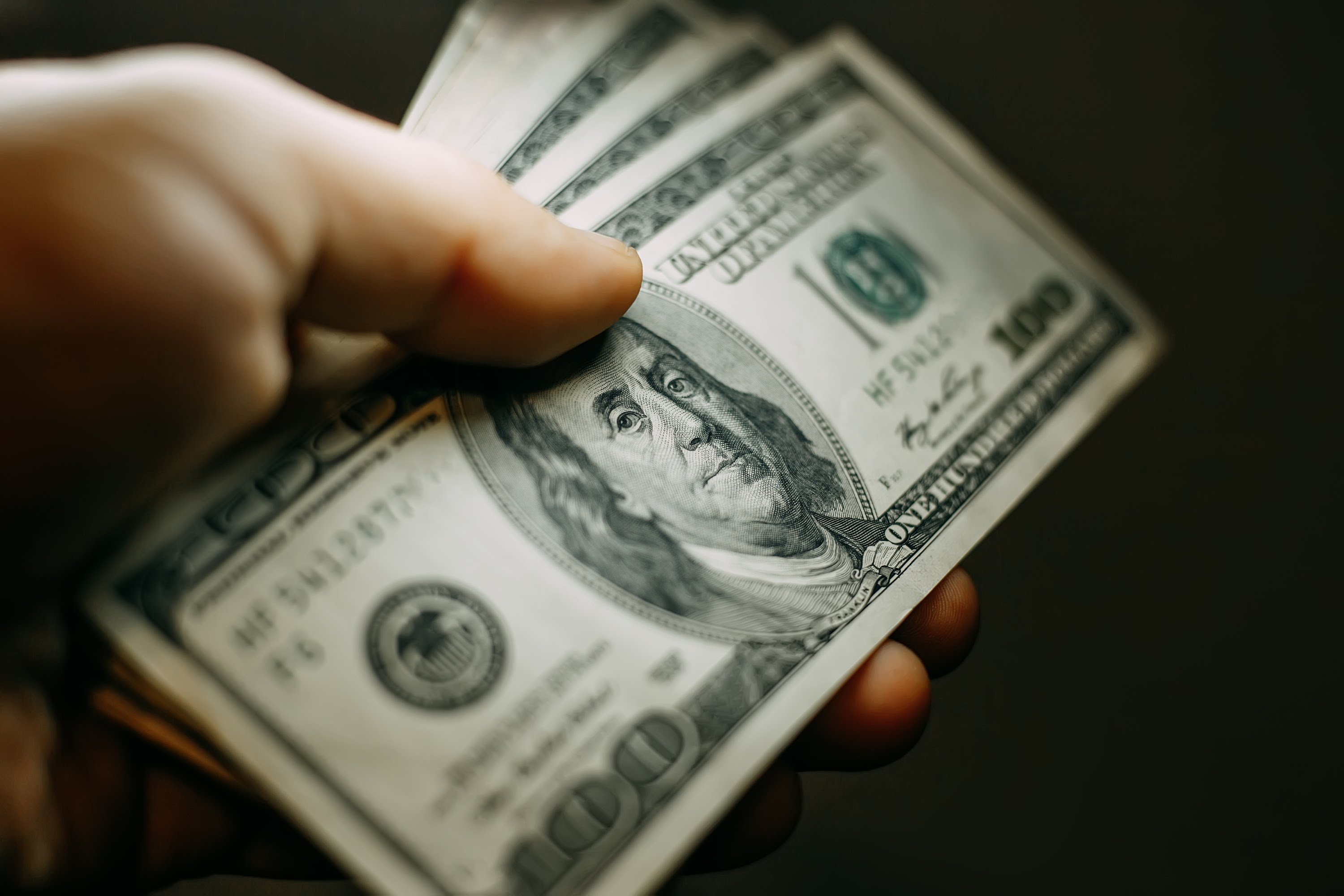 A hand holding a stash of one hundred dollar bills.