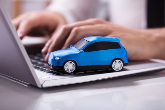 A small blue car model sits on a laptop