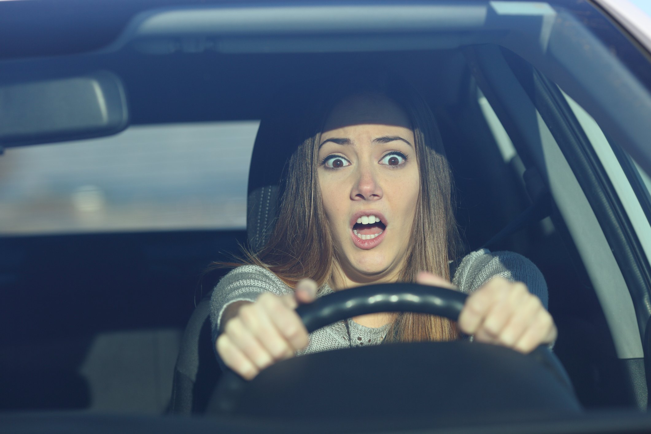 A surprised young woman driving a car.
