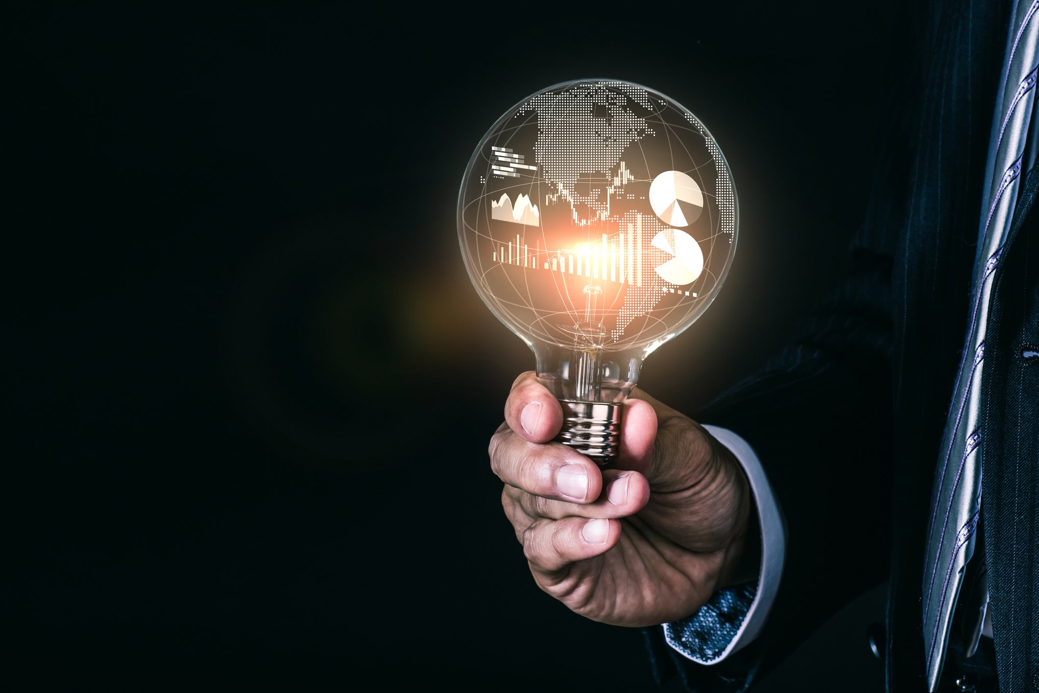 A person holding a light bulb with a globe and charts and graphs inside.