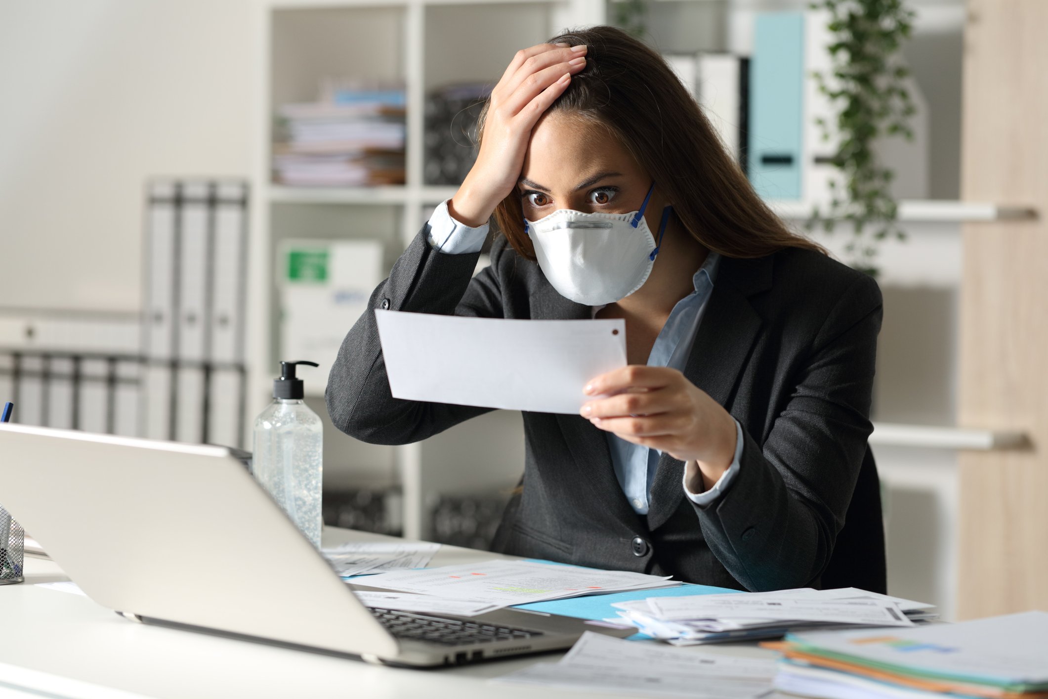 masked woman sitting at her laptop staring in disbelief at paper