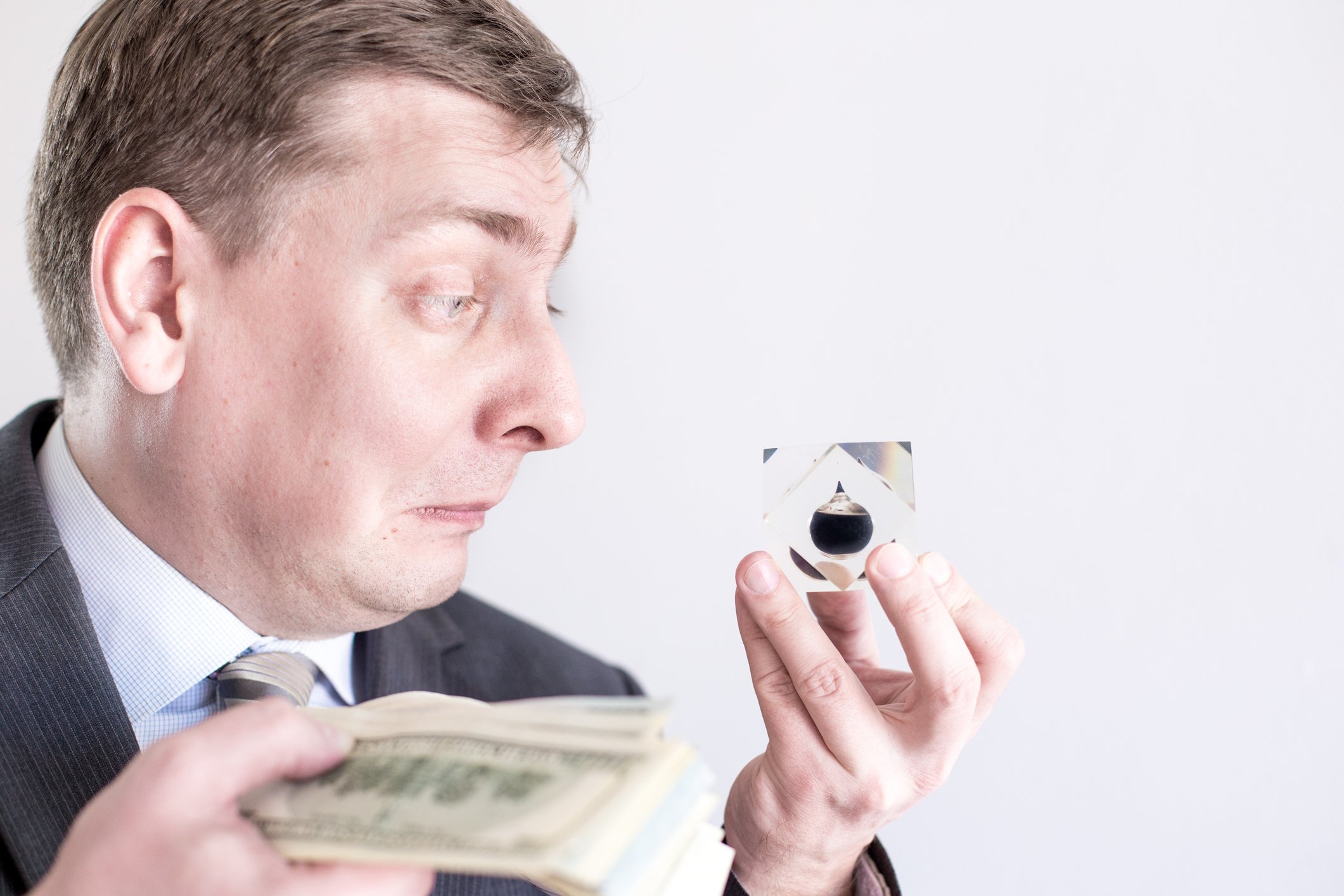 A man holds an oil droplet icon in one hand and a stack of paper currency in another.