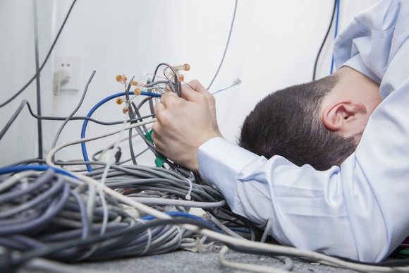 A man lowers his head to the ground, clutching a mess of disconnected network cables.