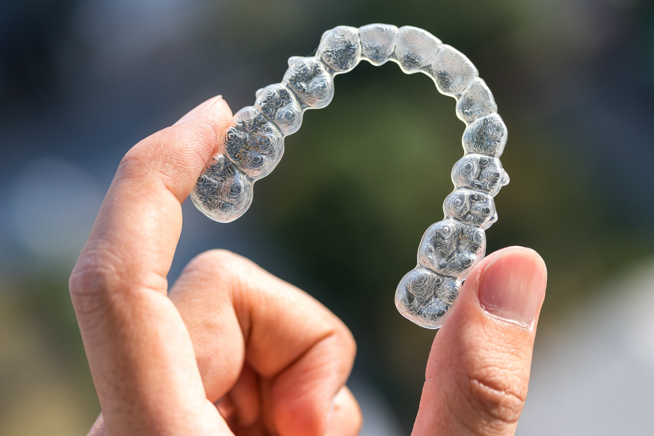 Hand holding clear dental aligner.