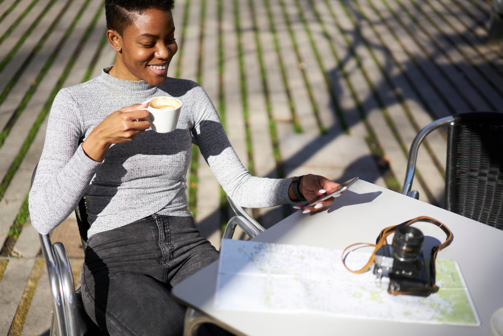 Young woman smiling at phone as she drinks coffee.