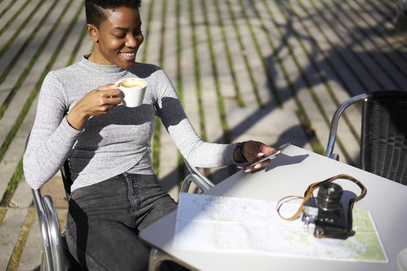 Young woman smiling at phone as she drinks coffee.