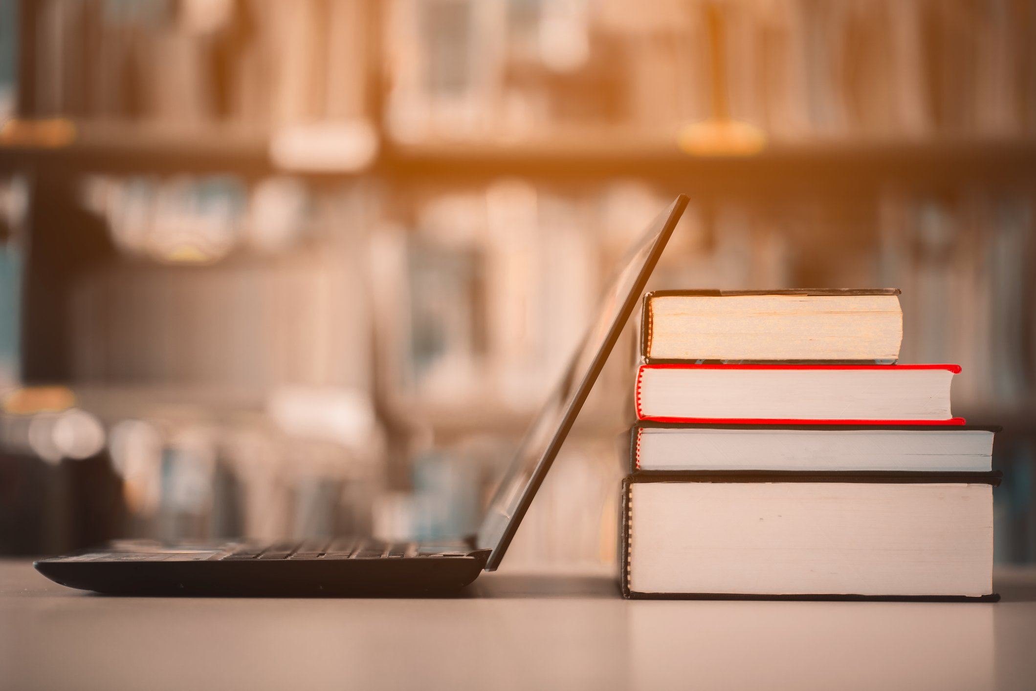 A laptop and a pile of books on a table in a library