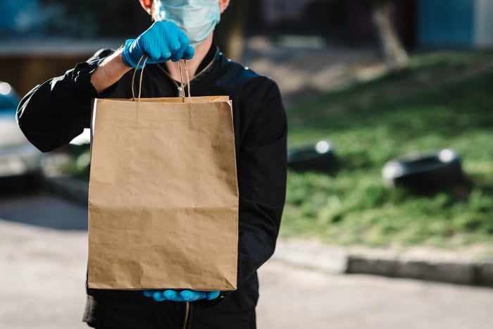 A man wearing a mask and gloves making a food delivery