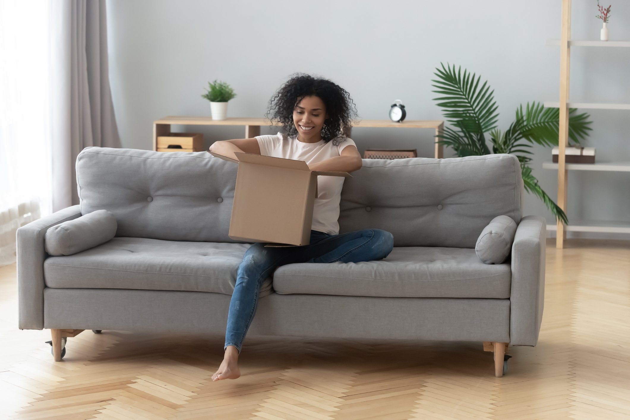 A woman sitting on a sofa and opening a box