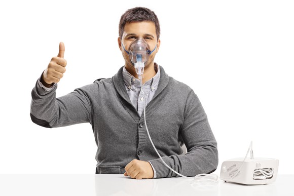 Man wearing a nebulizer mask and holding his thumb up