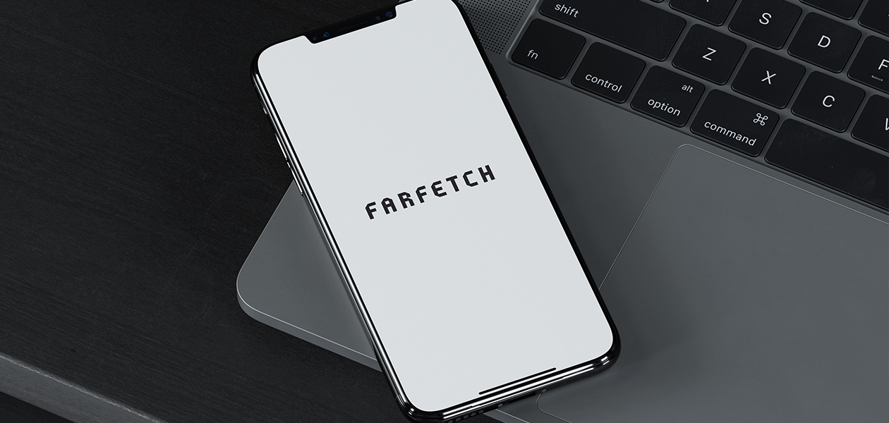 An iPhone with the Farfetch app open, resting on a laptop computer. 