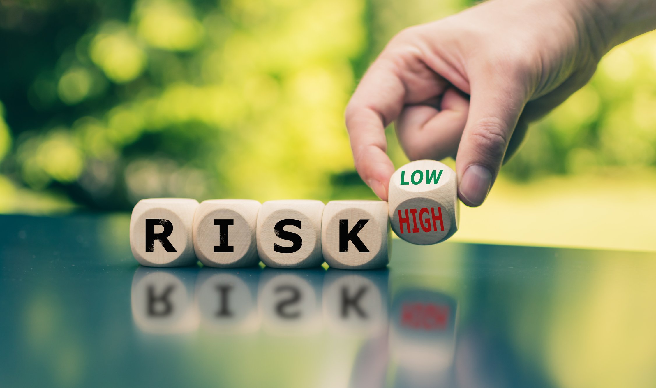 A row of dice spelling out the word Risk with a hand holding a final die in the position between the words Low and High