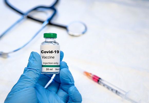A gloved hand holds a vial of coronavirus vaccine.