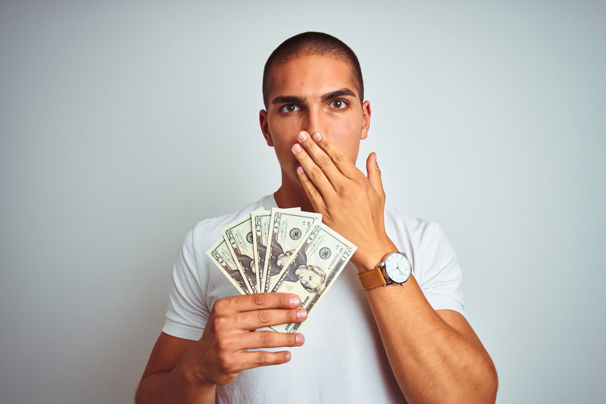 Man covering his mouth in embarrassment while holding five $20 bills.