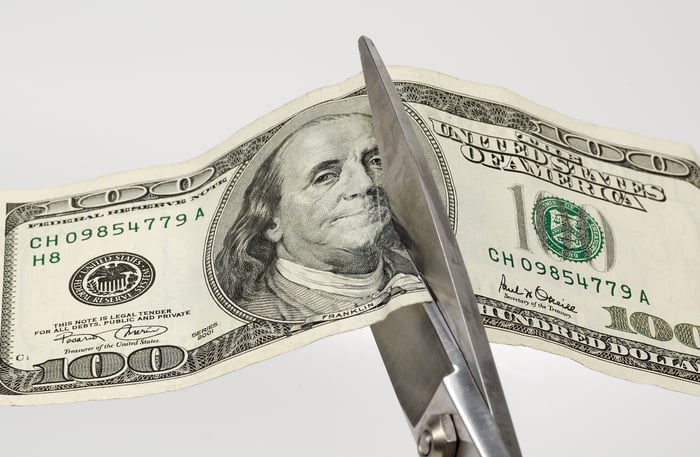 Scissors cutting through a one hundred dollar bill.