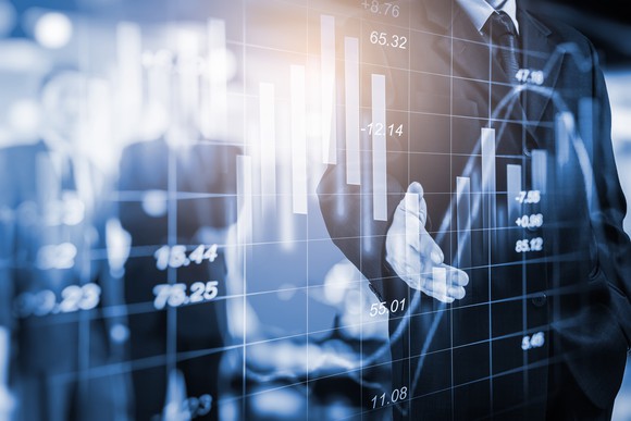 a man in suit behind a graphic showing charts insinuating stock price movements. 
