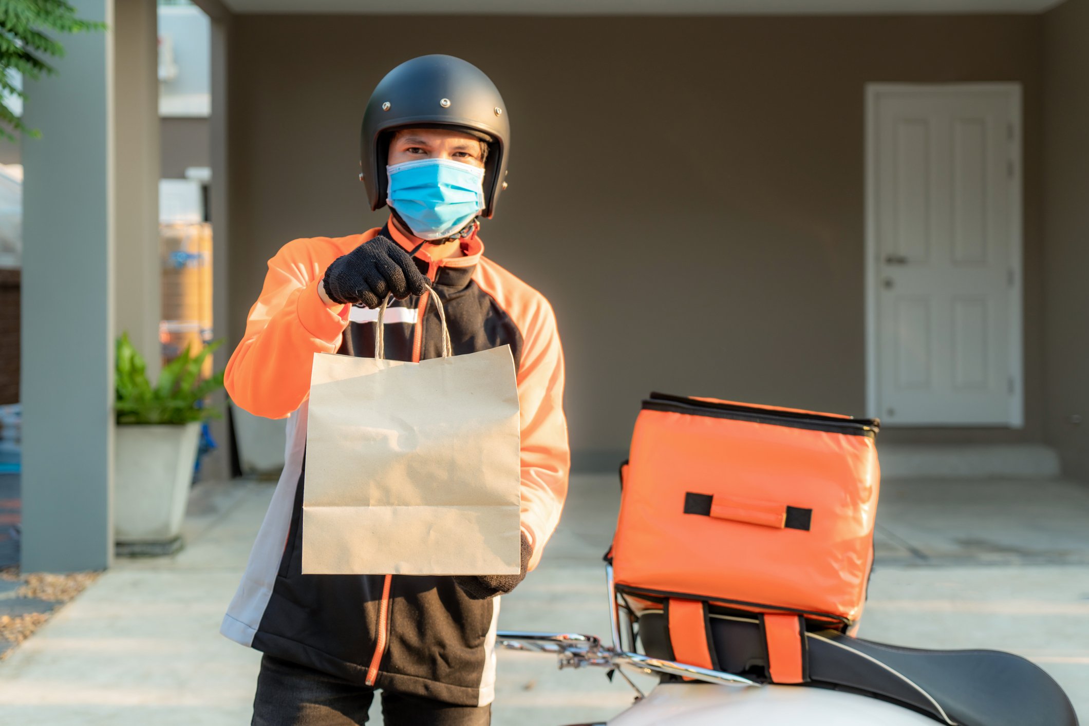 Masked food delivery driver holding a bag of food.