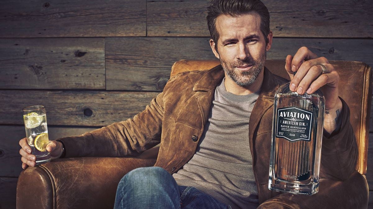 ryan reynolds in chair promoting aviation american gin bottle in his hand