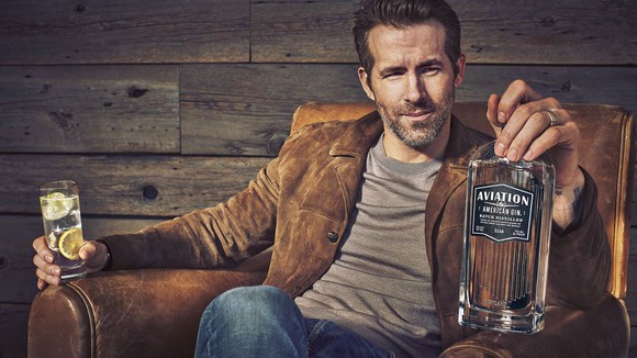 ryan reynolds in chair promoting aviation american gin bottle in his hand