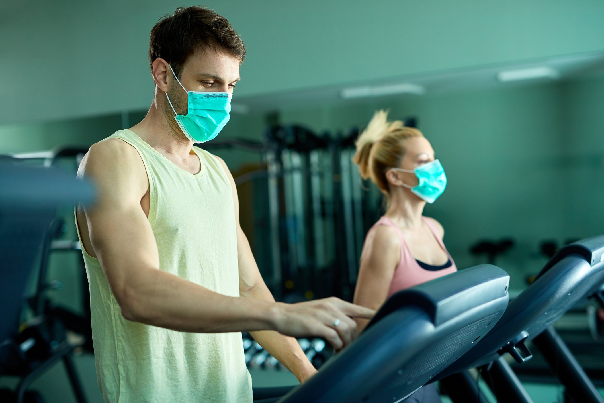 Two people in a gym working out while wearing masks. 