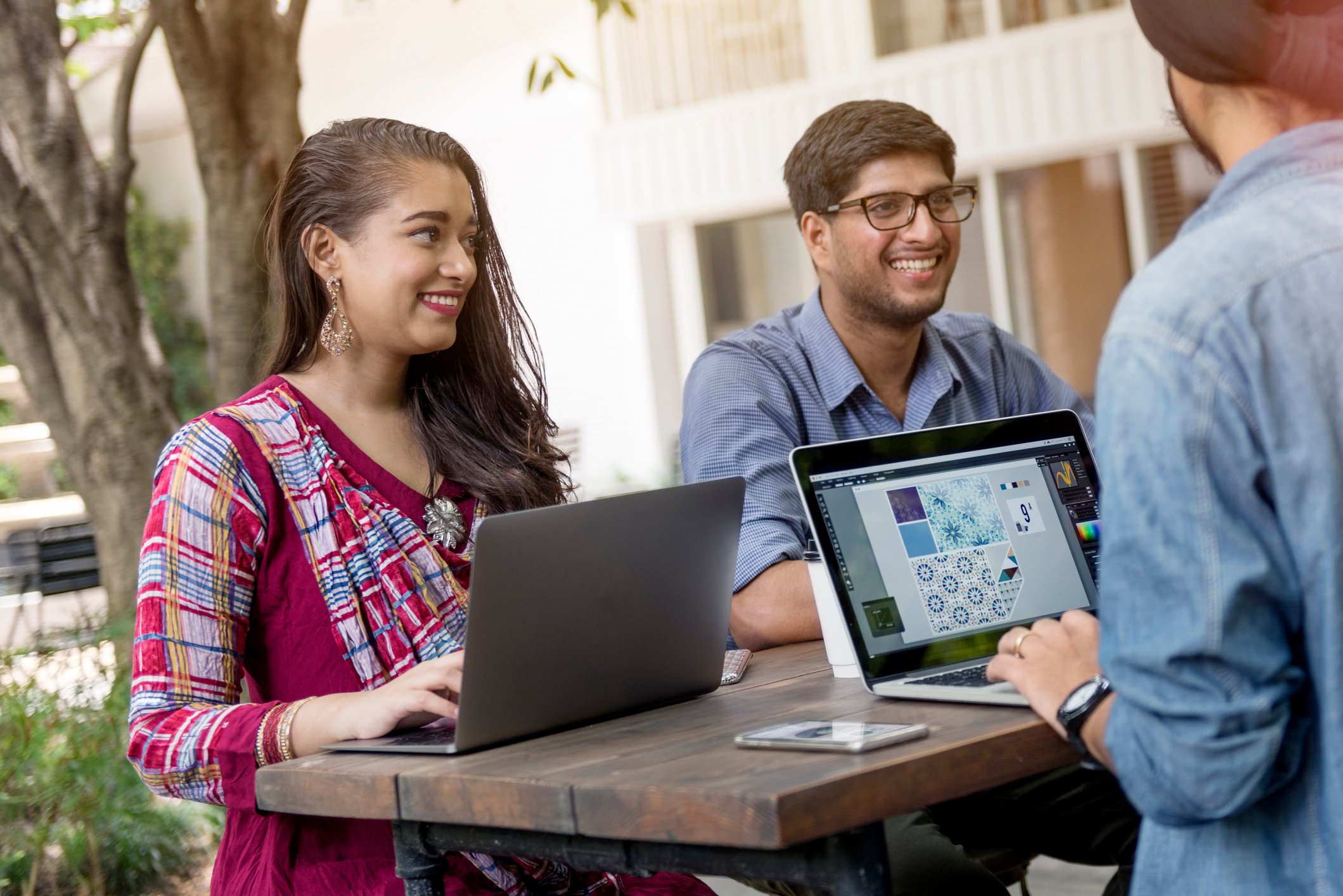 Young people in India gathered at an outdoor table using laptops.