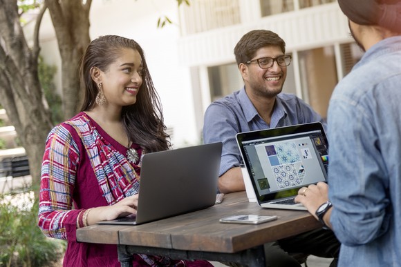 Young people in India gathered at an outdoor table using laptops.