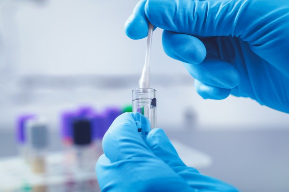 A person wearing gloves is placing a swab in a laboratory test vial.