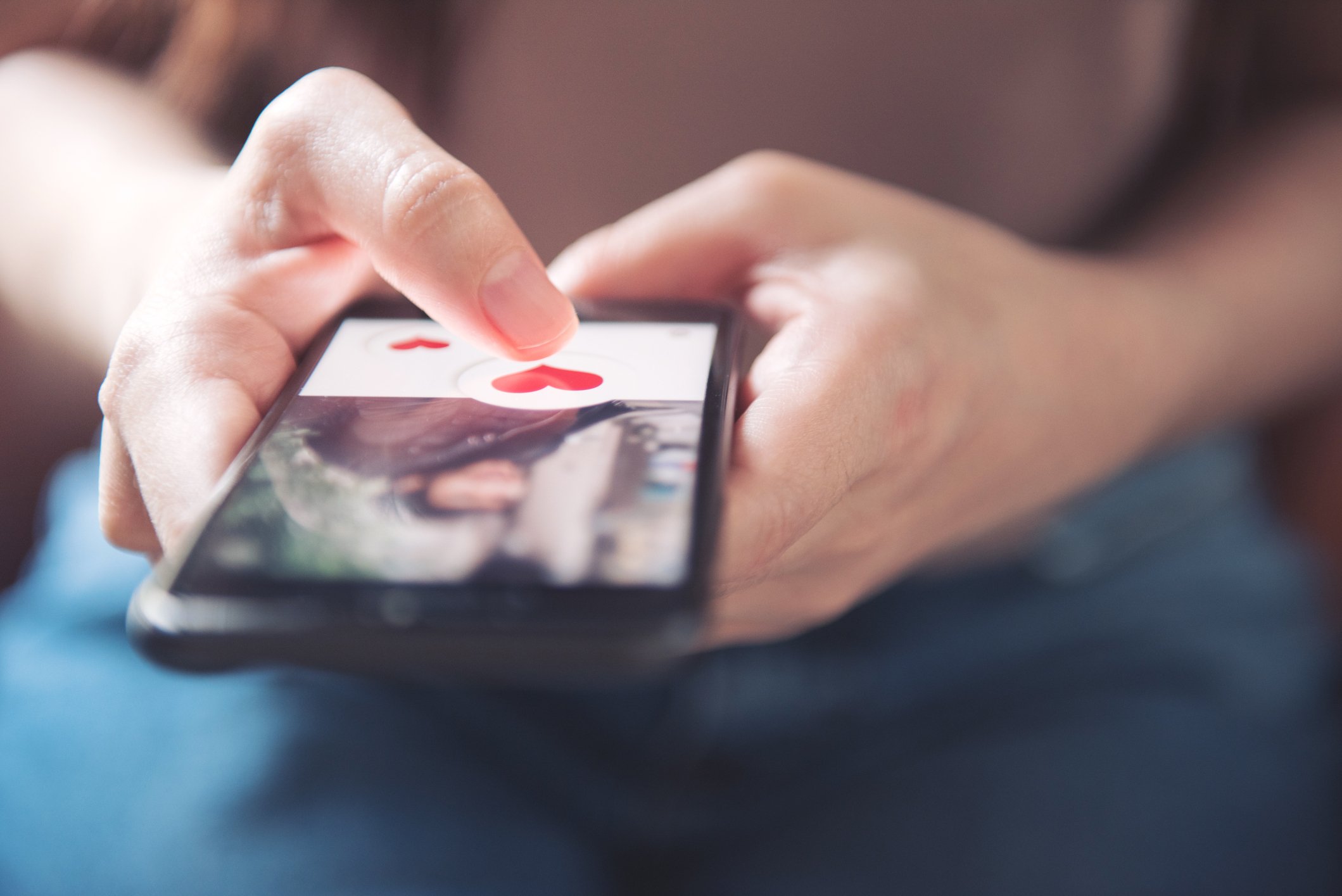 A person using a smartphone on which there is a picture of a person and red cartoon hearts