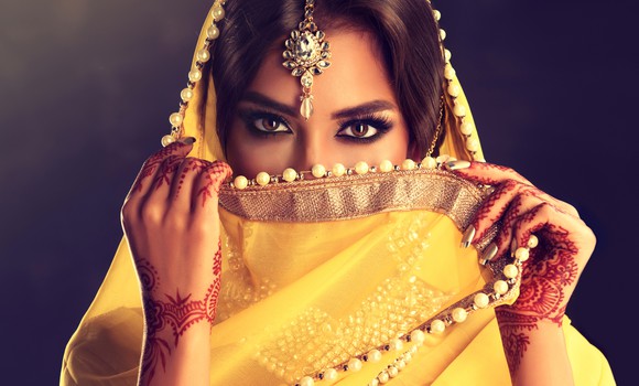 An Indian woman with henna on her hands and a yellow scarf partially covering her face.