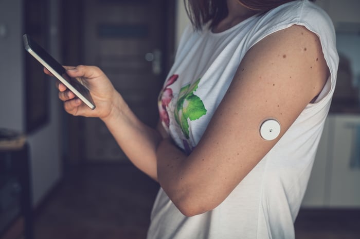 Woman wearing a glucose monitor and looking at smartphone.