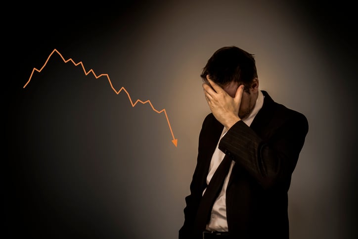 An exasperated businessman standing next to a falling stock chart.
