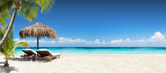 A beach with pale sand and two chaises set up under a thatched umbrella