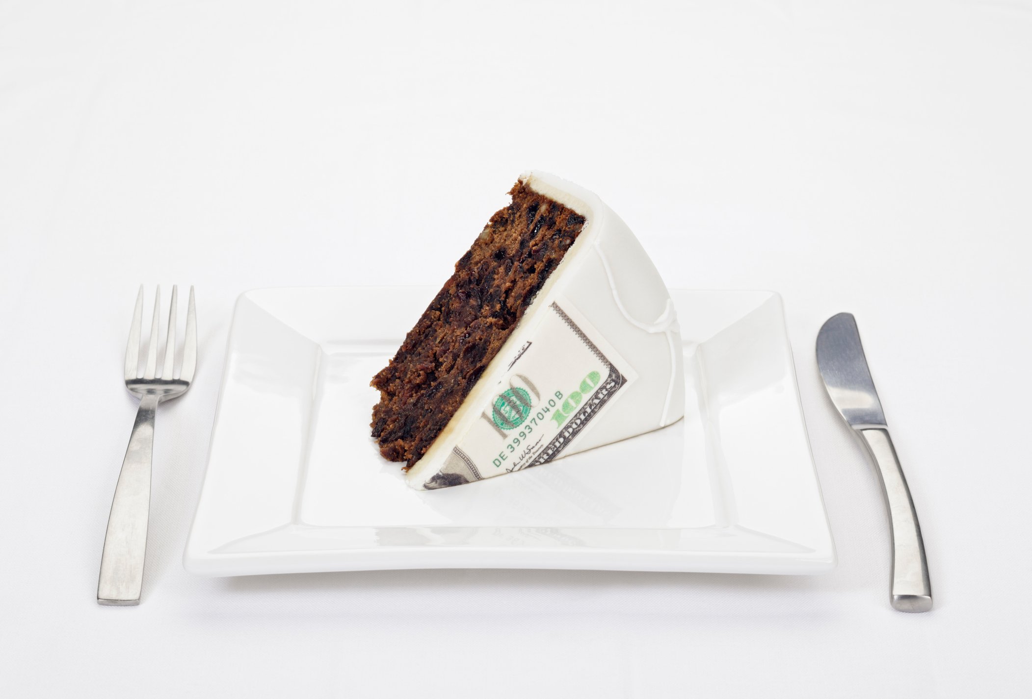 Huge slice of cake served on a plate with a hundred dollar bill printed on the frosting.
