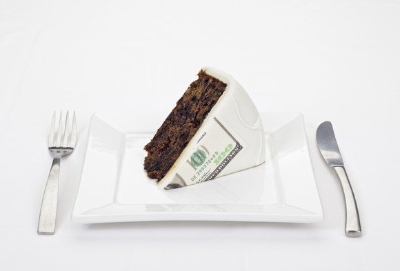Huge slice of cake served on a plate with a hundred dollar bill printed on the frosting.