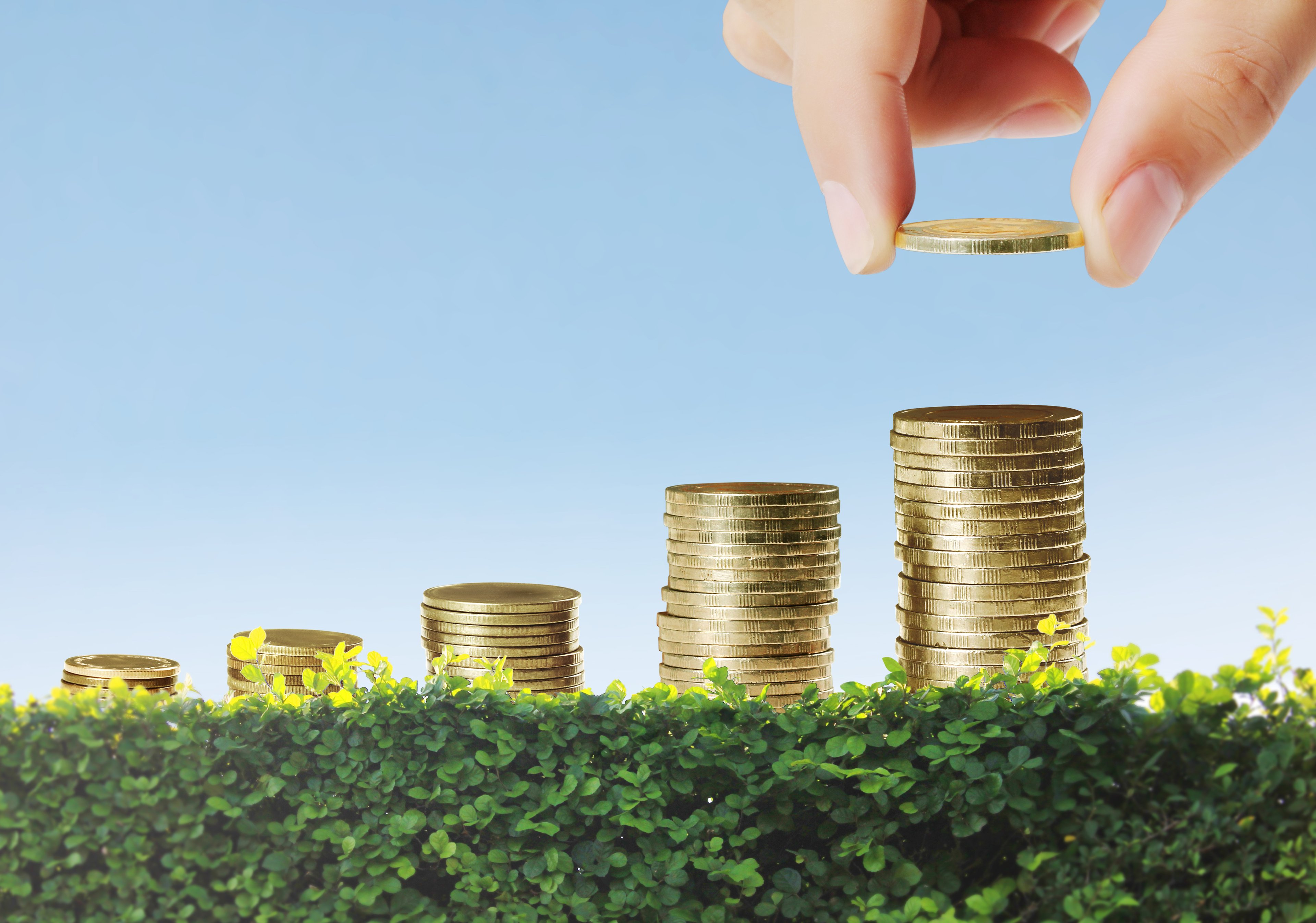 Multiple ascending stacks of coins, with a person placing a coin atop the tallest stack.
