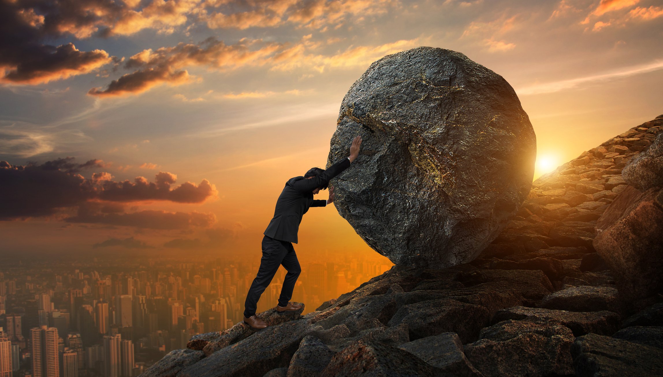 A businessman pushes a boulder uphill. 